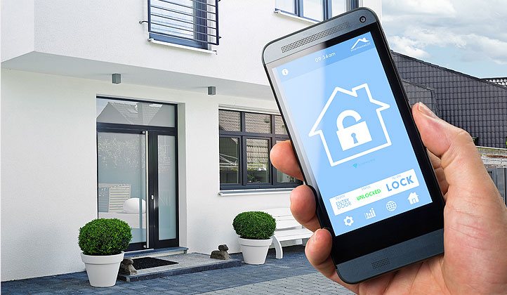 Smart-Home-Anwendungen machen vieles möglich! Wir beraten Sie gerne! Ein Smartphone mit einer Heimsteuerungs-Applikation vor einem Einfamilienhaus